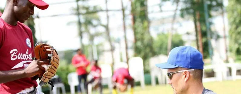 A young Nigerian player with a fielding glove receiving instruction from a coach during a training session