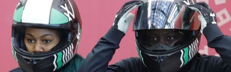 Two Nigerian bobsledders wearing green and white helmets at the start area