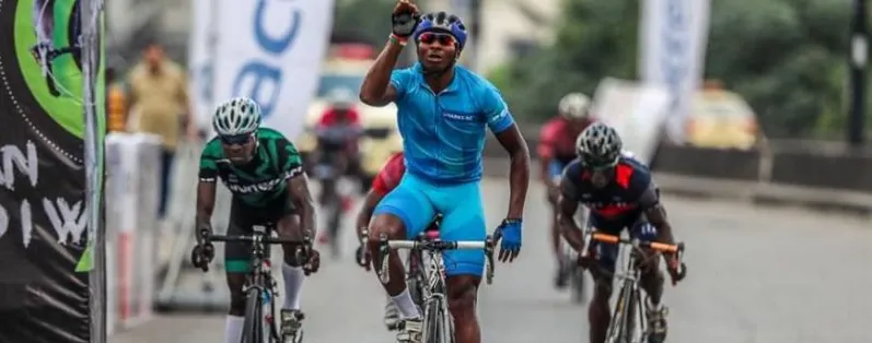 A Nigerian cyclist raising his fist as he wins a road race, with other riders behind him