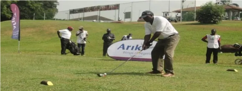 A golfer addressing the ball on a Nigerian course, with caddies and players waiting behind him