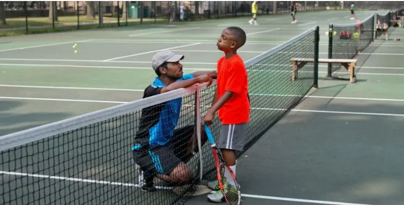 A coach talking to a young player at the net on a Nigerian court