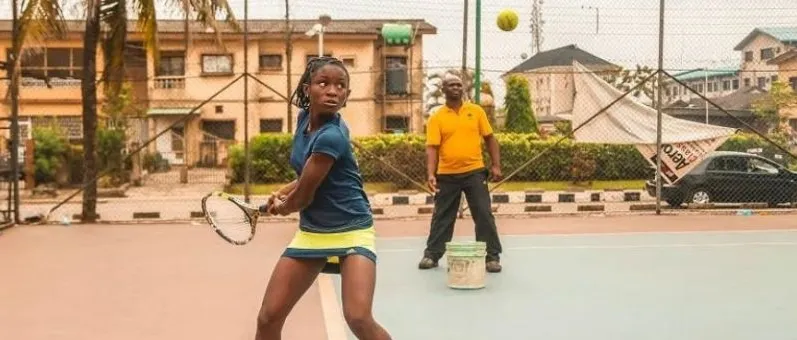 A young Nigerian girl practising on a Lagos court with her coach