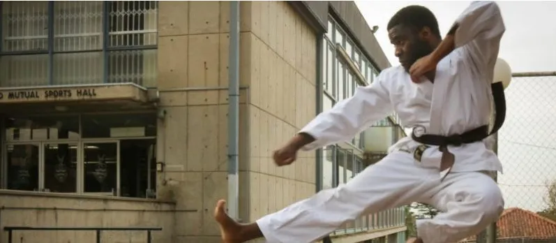 A Nigerian karateka performing a high kick outside a sports hall