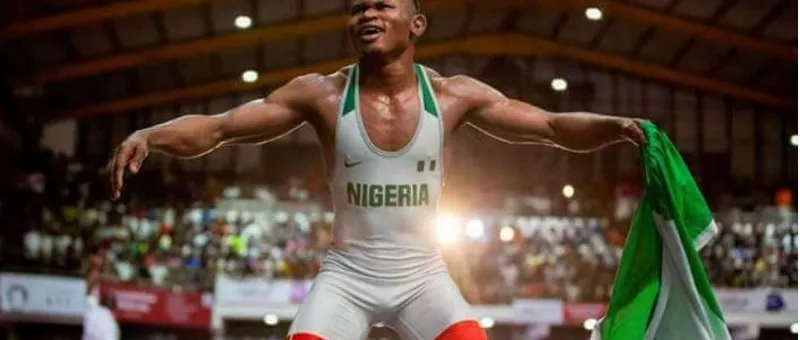 A Nigerian wrestler in a white Nigeria singlet celebrating with the green and white flag